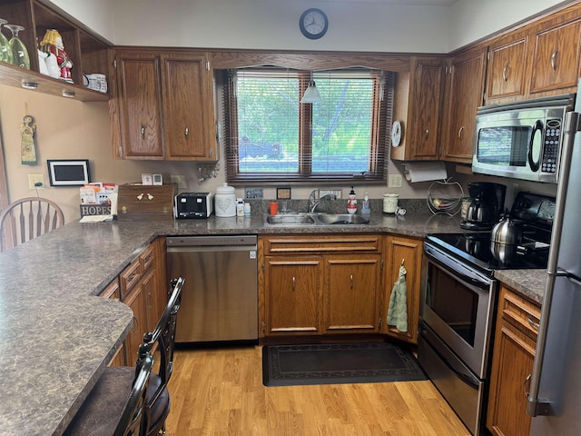 1130 8th St, Minot, ND 58703 - kitchen featuring stainless steel appliances, a sink, light wood-type flooring, a peninsula, and brown cabinetry