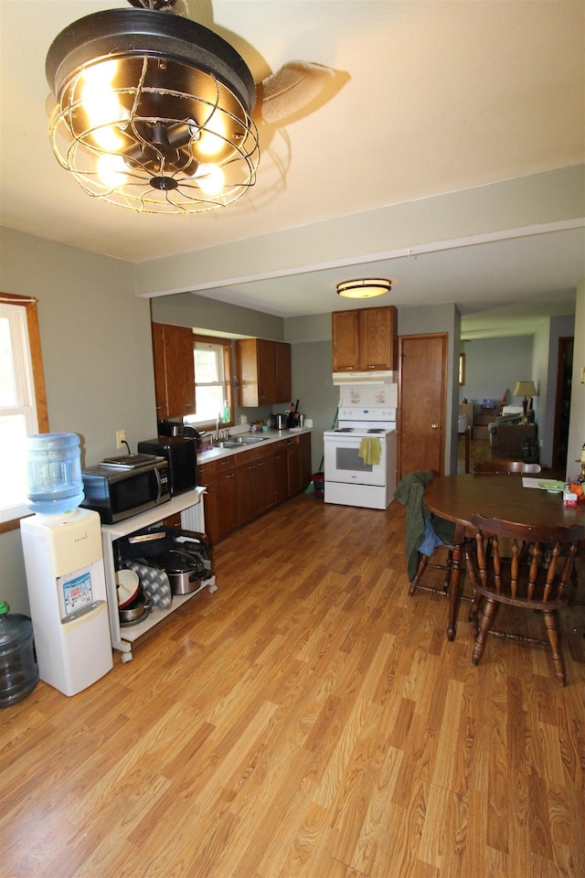 506 W Ave, Granville, ND 58741 - kitchen with electric stove, brown cabinets, a sink, light wood finished floors, and a chandelier