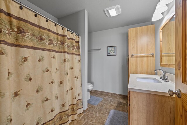 1164 100th St, Bottineau, ND 58318 - bathroom with vanity, toilet, stone finish floors, baseboards, and curtained shower