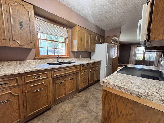 1107 SE 2nd St, Minot, ND 58701 - kitchen featuring a sink, white appliances, a textured ceiling, light countertops, and brown cabinetry