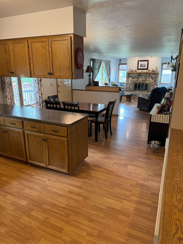919 9th St, Minot, ND 58703 - kitchen featuring light wood-type flooring, dark countertops, brown cabinets, a textured ceiling, and a stone fireplace