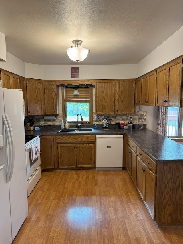 919 9th St, Minot, ND 58703 - kitchen with white appliances, a sink, brown cabinets, a peninsula, and light wood-style flooring