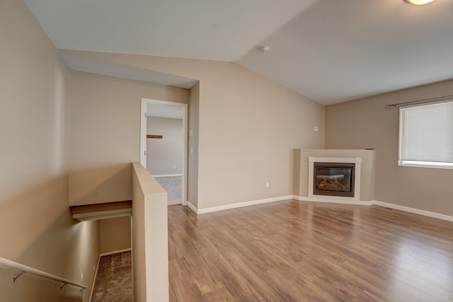 3328 NW 20th Ave, Minot, ND 58703 - unfurnished living room featuring lofted ceiling, wood finished floors, a glass covered fireplace, and baseboards