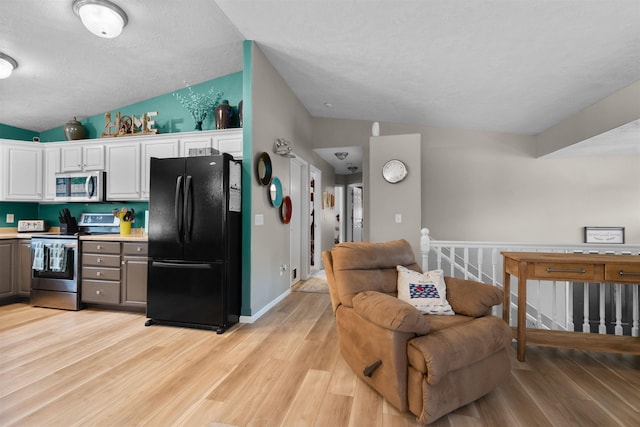 1705 SW Evergreen Ave, Minot, ND 58701 - kitchen with appliances with stainless steel finishes, vaulted ceiling, light wood finished floors, white cabinetry, and light countertops