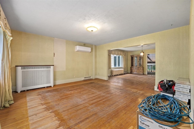 306 2nd St, Towner, ND 58788 - unfurnished living room featuring radiator, a wall mounted air conditioner, wallpapered walls, light wood-style flooring, and baseboard heating