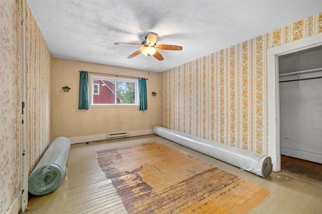 306 2nd St, Towner, ND 58788 - unfurnished bedroom with hardwood / wood-style flooring, wallpapered walls, a textured ceiling, a ceiling fan, and a baseboard heating unit