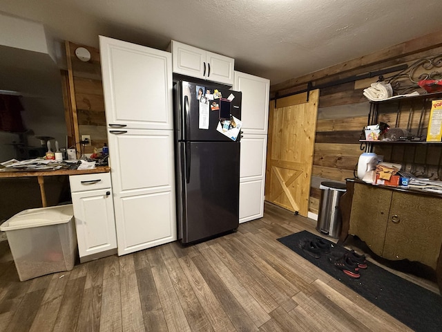 3301 SE 1st St, Minot, ND 58701 - kitchen with freestanding refrigerator, a barn door, wooden walls, dark wood finished floors, and white cabinetry