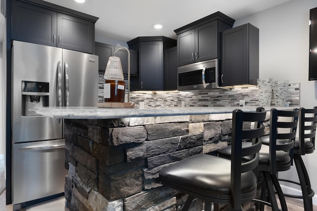 2009 35th Ave, Minot, ND 58701 - kitchen with appliances with stainless steel finishes, backsplash, a kitchen bar, recessed lighting, and light stone countertops