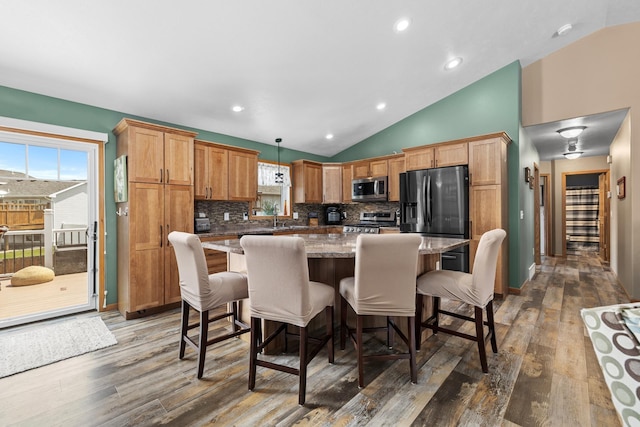 1808 28th St, Minot, ND 58703 - kitchen featuring appliances with stainless steel finishes, lofted ceiling, hardwood / wood-style floors, tasteful backsplash, and a kitchen island