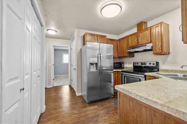 606 19th Ave Unit 7, Minot, ND 58701 - kitchen with stainless steel appliances, under cabinet range hood, brown cabinets, light countertops, and dark wood-style floors
