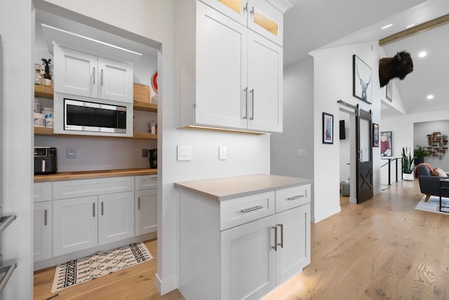 2415 43rd Ave, Minot, ND 58701 - kitchen with a barn door, stainless steel microwave, open shelves, light wood finished floors, and white cabinets