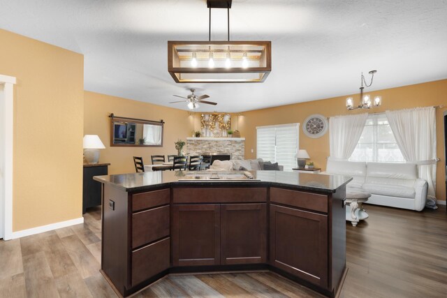 4007 Crossing St, Minot, ND 58701 - kitchen featuring open floor plan, ceiling fan, a chandelier, a kitchen island, and a stone fireplace