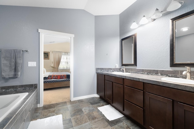 4007 Crossing St, Minot, ND 58701 - bathroom with vaulted ceiling, connected bathroom, double vanity, tiled tub, and stone finish floors