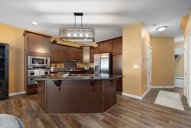 4007 Crossing St, Minot, ND 58701 - kitchen with stainless steel appliances, dark countertops, a breakfast bar, dark wood-type flooring, and an island with sink
