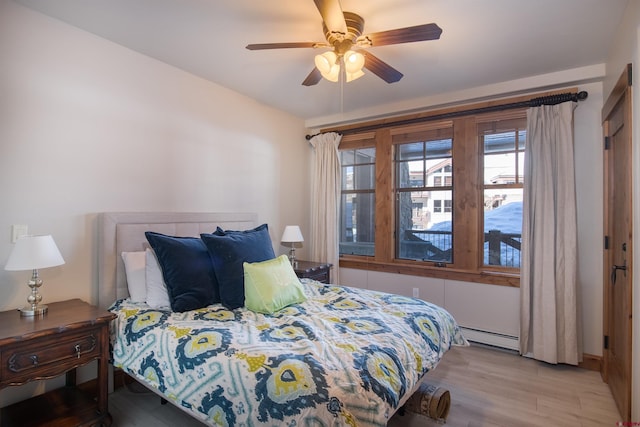 bedroom with ceiling fan, light wood-type flooring, and a baseboard heating unit