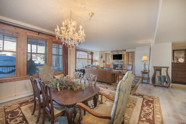 dining space with light hardwood / wood-style flooring, baseboard heating, a stone fireplace, and a chandelier