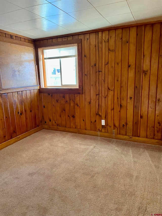 carpeted empty room featuring wooden walls and a drop ceiling