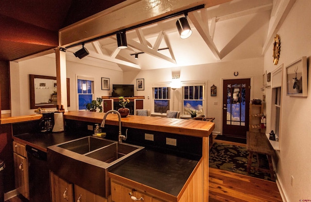 kitchen with sink, lofted ceiling with beams, black dishwasher, track lighting, and dark wood-type flooring