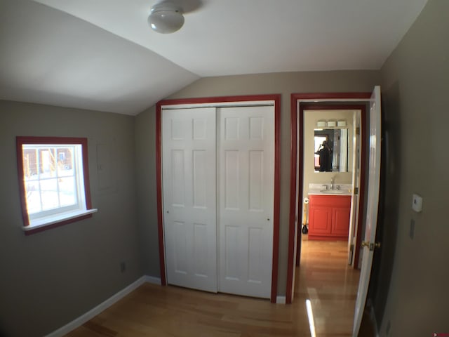 unfurnished bedroom featuring vaulted ceiling, a closet, light wood-type flooring, and sink