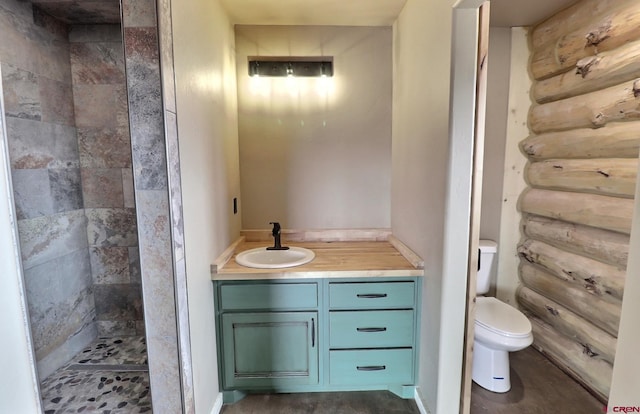 bathroom with toilet, a tile shower, and vanity