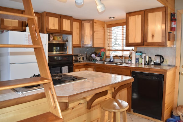 kitchen with tasteful backsplash, light tile floors, tile countertops, black appliances, and sink