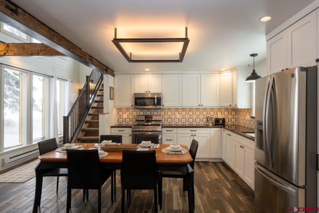 kitchen with hanging light fixtures, white cabinetry, dark hardwood / wood-style floors, appliances with stainless steel finishes, and beam ceiling