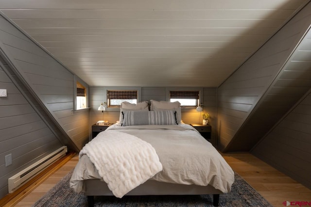 bedroom with lofted ceiling, wood walls, light wood-type flooring, and a baseboard heating unit