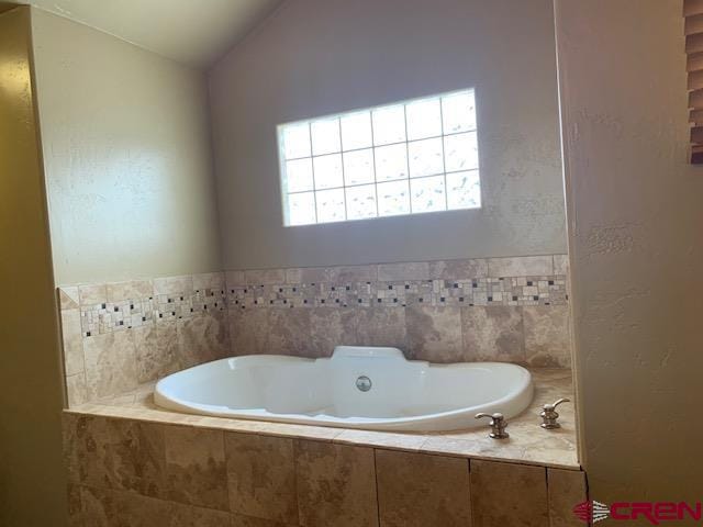 bathroom featuring a relaxing tiled bath and vaulted ceiling