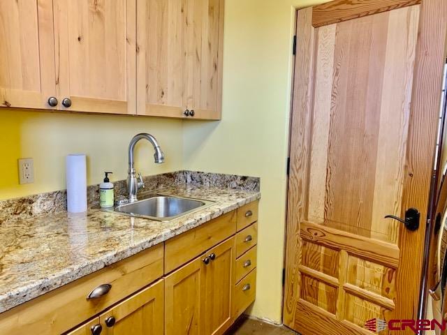 kitchen with light brown cabinetry, sink, and light stone counters