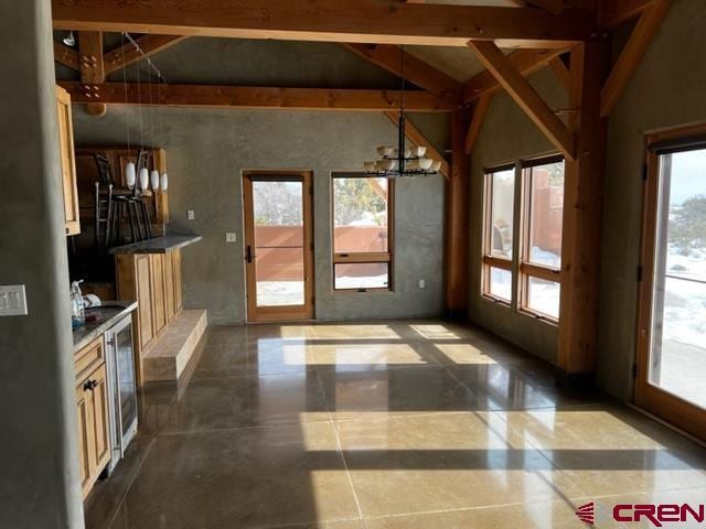 doorway to outside with an inviting chandelier, a healthy amount of sunlight, and vaulted ceiling with beams