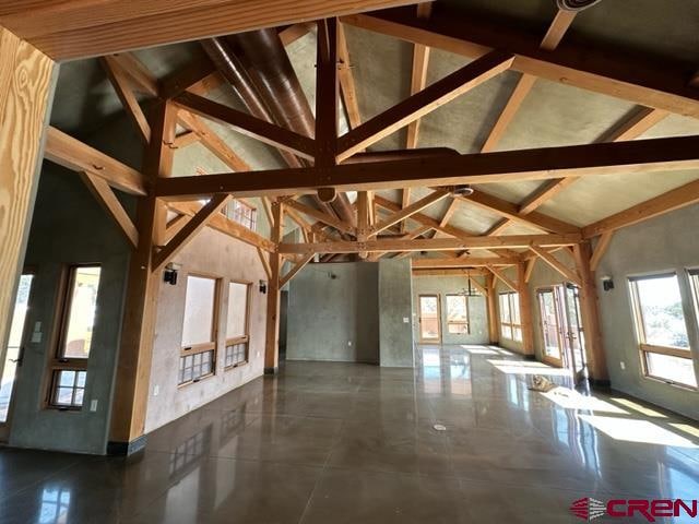 interior space featuring high vaulted ceiling, beam ceiling, and dark tile floors