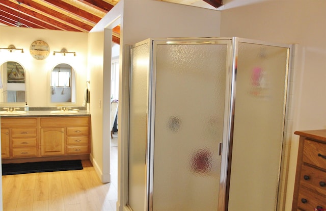 bathroom with dual sinks, vanity with extensive cabinet space, vaulted ceiling with beams, a shower with door, and wood-type flooring