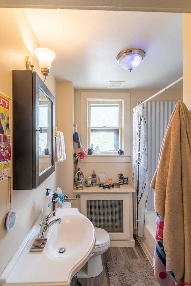 full bathroom featuring toilet, radiator heating unit, hardwood / wood-style floors, shower / tub combo with curtain, and sink