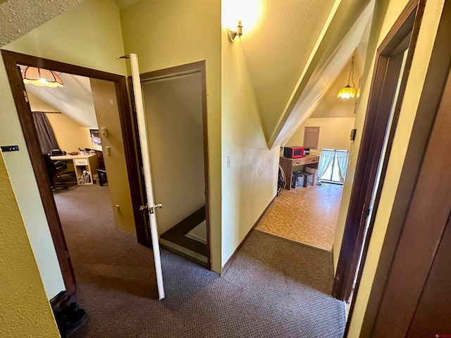 corridor featuring lofted ceiling, dark carpet, and a textured ceiling