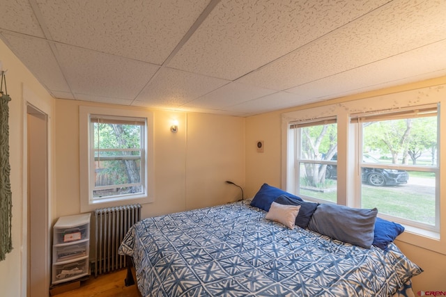 bedroom featuring a paneled ceiling, radiator heating unit, and hardwood / wood-style flooring