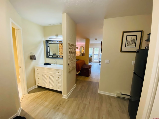 corridor featuring baseboard heating, sink, and light hardwood / wood-style floors