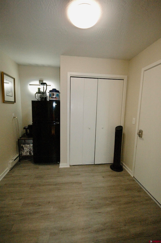 unfurnished bedroom featuring a baseboard heating unit, light wood-type flooring, and black fridge