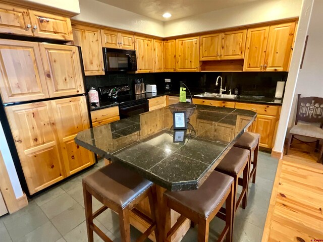 kitchen featuring a breakfast bar area, backsplash, light tile floors, sink, and black appliances