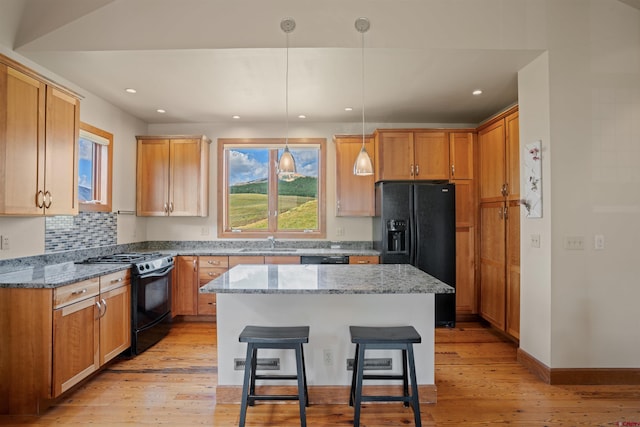 kitchen featuring light wood-type flooring, a kitchen island, a kitchen bar, decorative light fixtures, and black appliances