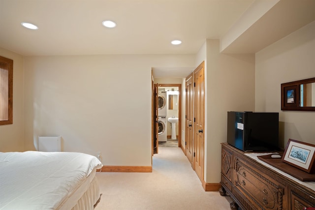 bedroom featuring light colored carpet, ensuite bath, and stacked washer / dryer