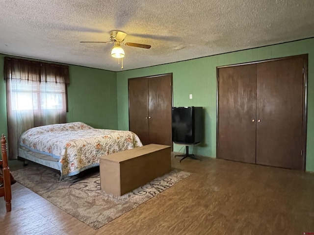 bedroom featuring multiple closets, ceiling fan, a textured ceiling, and hardwood / wood-style flooring