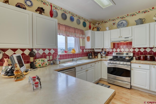 kitchen featuring appliances with stainless steel finishes, backsplash, sink, light hardwood / wood-style flooring, and white cabinets