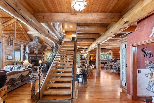 stairs with beamed ceiling, a notable chandelier, rustic walls, a fireplace, and light hardwood / wood-style flooring