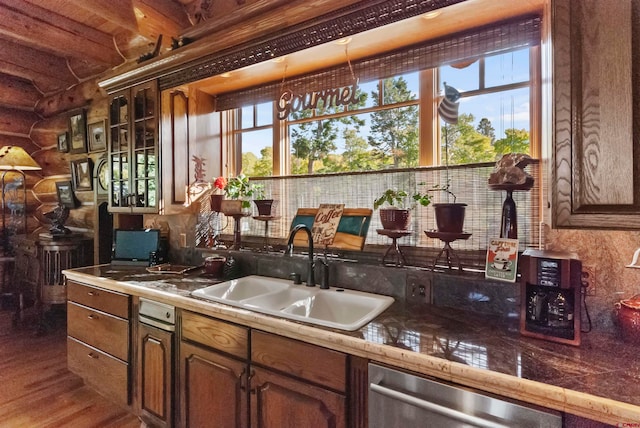 kitchen with rustic walls, dark hardwood / wood-style floors, beamed ceiling, sink, and stainless steel dishwasher