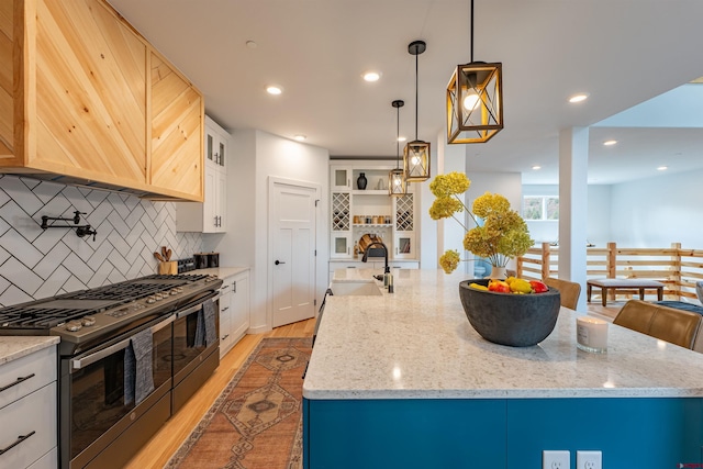 kitchen with an island with sink, pendant lighting, light wood-type flooring, tasteful backsplash, and range with two ovens