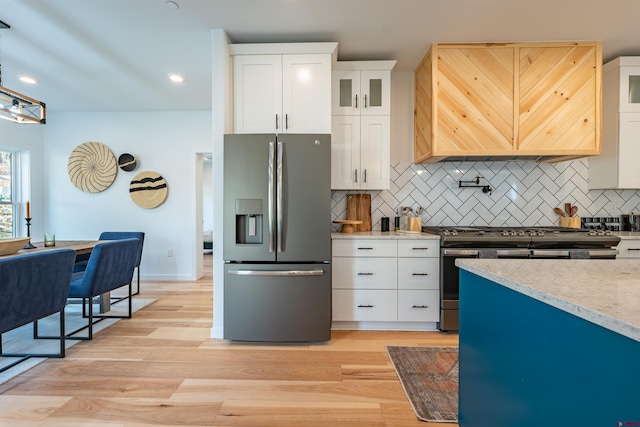 kitchen featuring appliances with stainless steel finishes, light hardwood / wood-style flooring, light stone countertops, tasteful backsplash, and white cabinetry