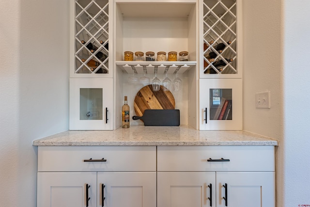 bar with white cabinets and light stone countertops