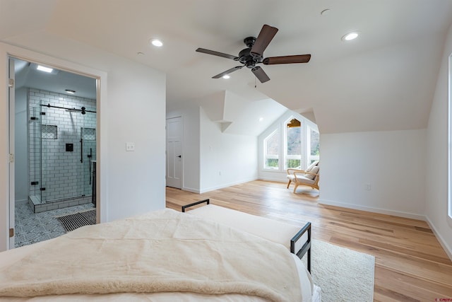 bedroom with a barn door, light wood-type flooring, ceiling fan, connected bathroom, and vaulted ceiling