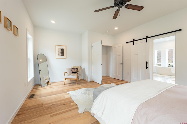 bedroom with a barn door, multiple windows, ceiling fan, and light hardwood / wood-style flooring