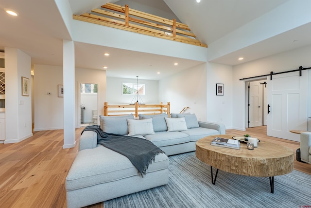 living room with a barn door, high vaulted ceiling, and light wood-type flooring